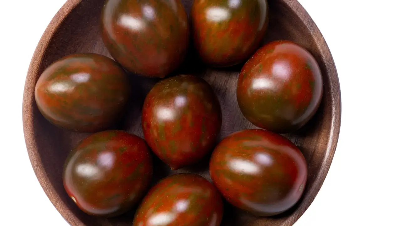 Close-up of small, oval cherry tomatoes showing a rich reddish-brown color with dark green stripes and glossy skin in a wooden bowl on a white background.